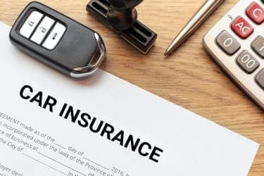 Paper reading 'car insurance' on a table, beside a set of car keys, a pen, and a calculator.